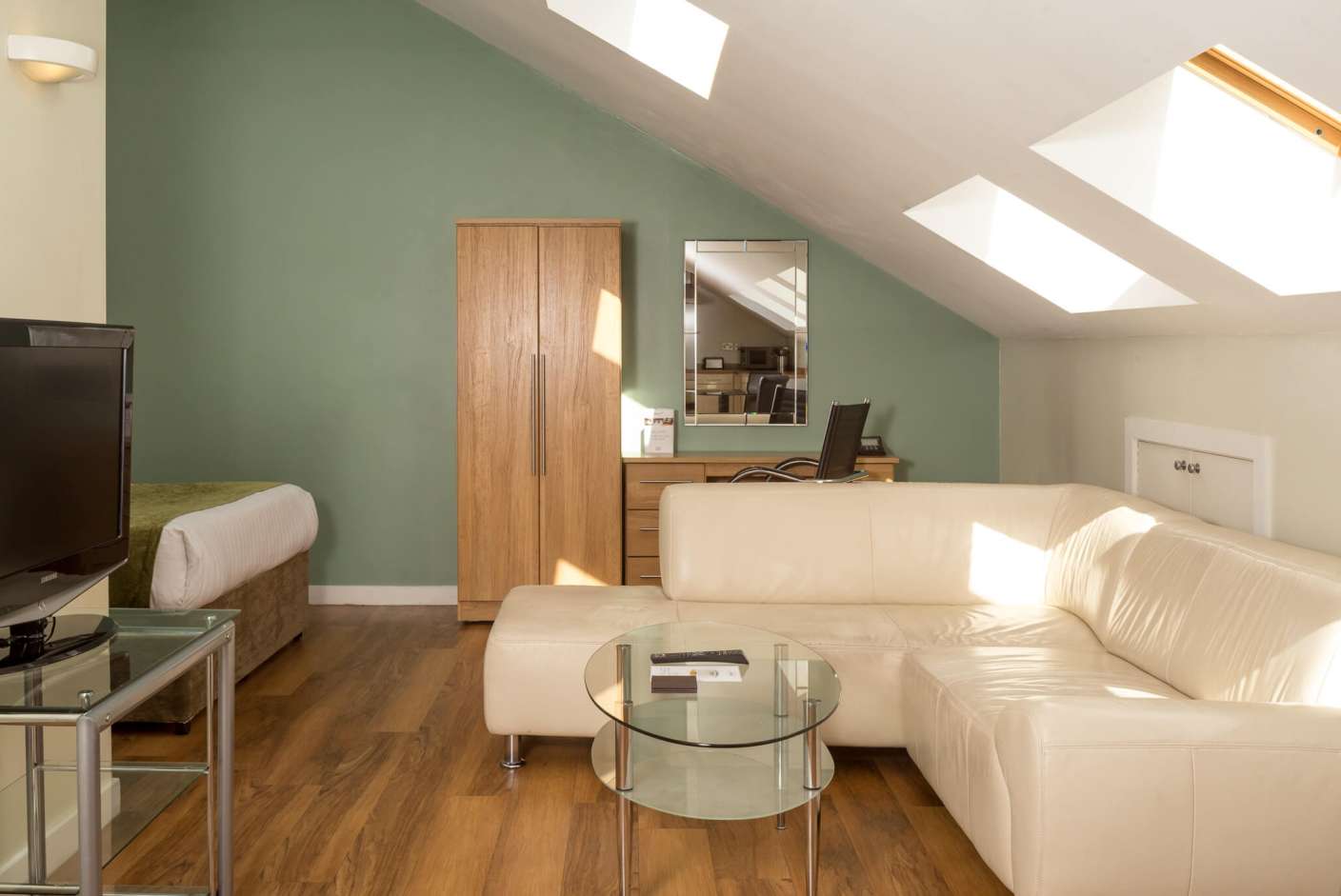 Living area with white leather L shaped couch, Desk, chair and TV.