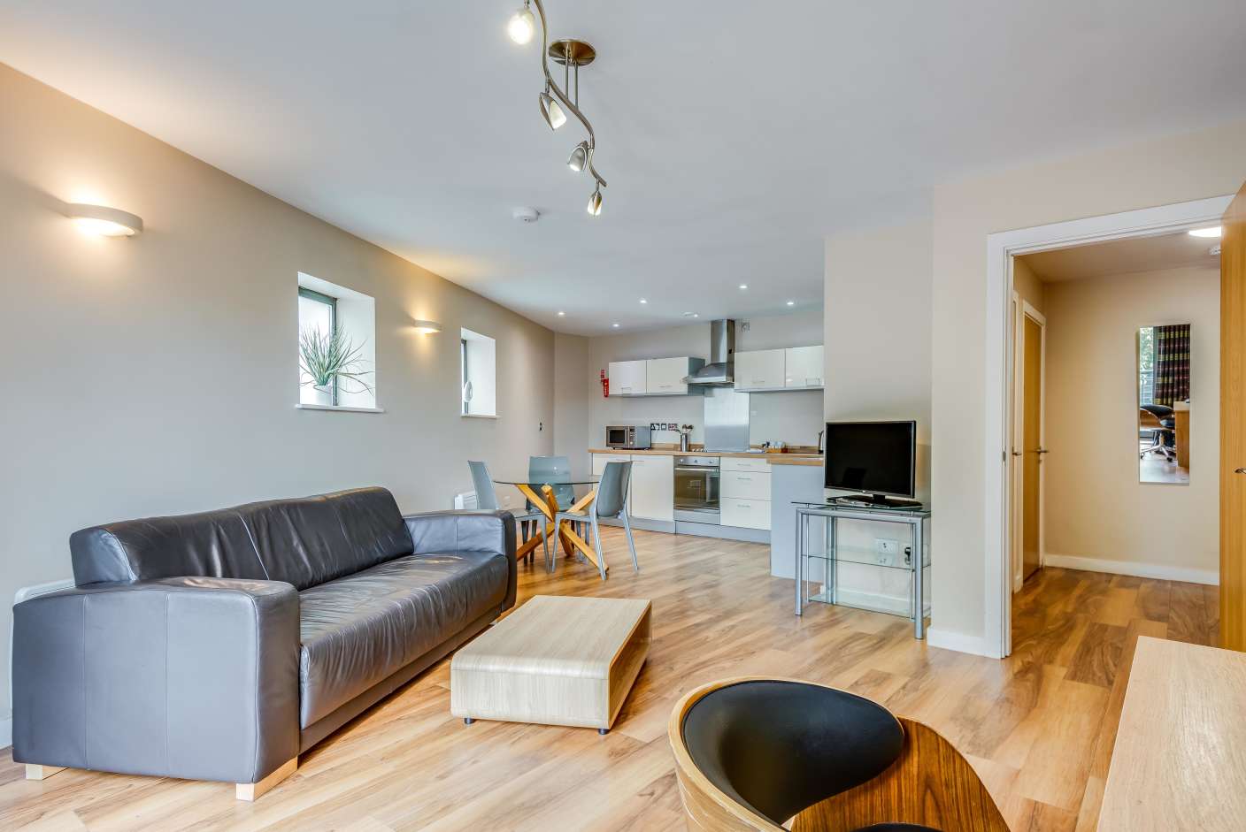 Spacious apartment kitchen and living area with faux leather sofa, dining table, tv and fully equipped kitchen