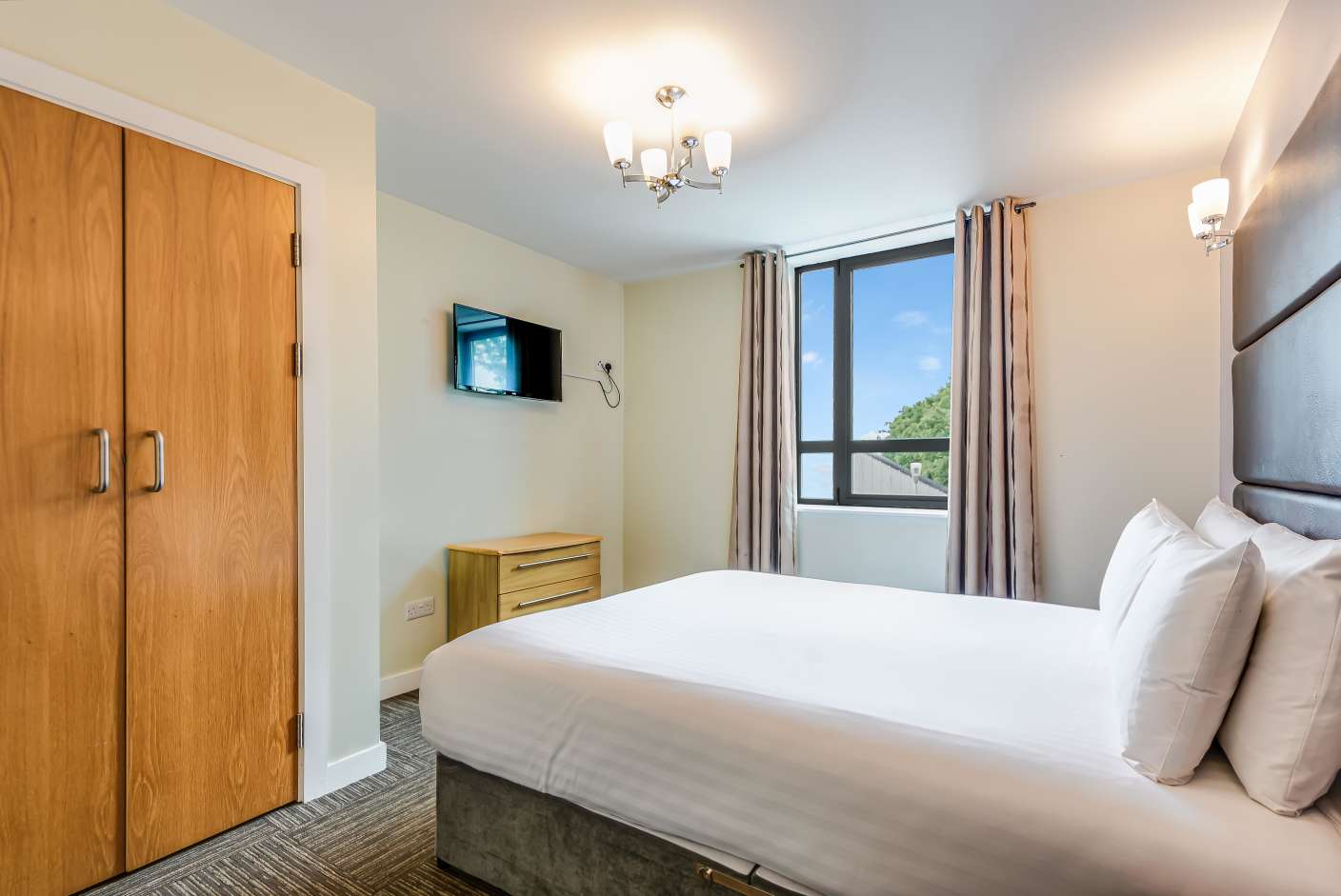 Spacious apartment bedroom with king side bed, wardrobe, chest of drawers and TV.