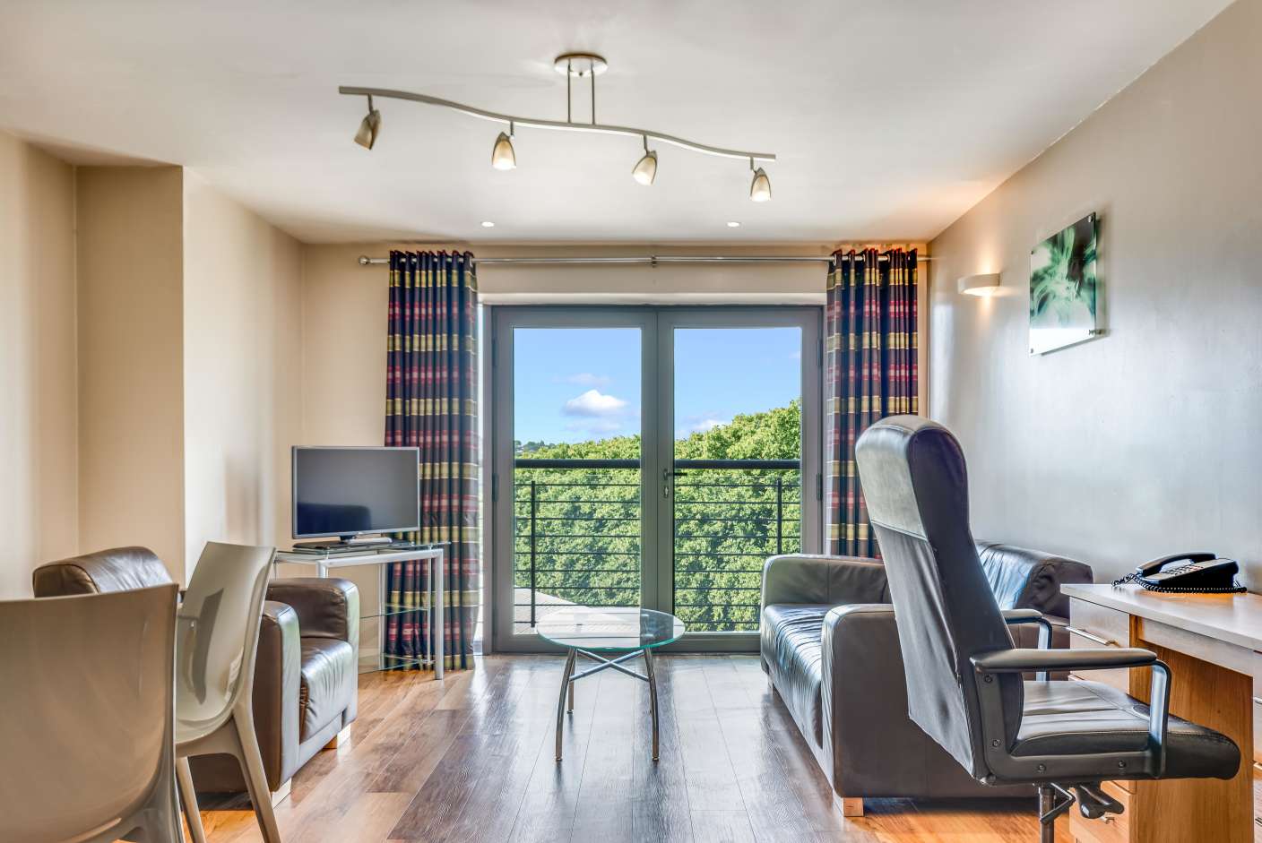 Apartment living area with brown sofa, wooden floors, TV and Juliet balcony