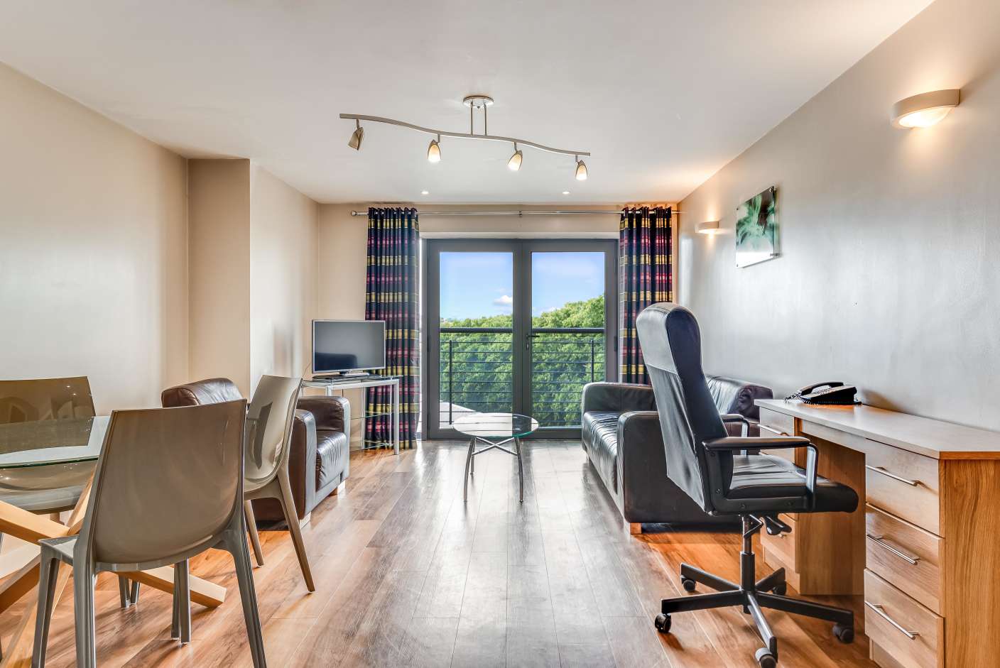 Apartment living area with brown sofa, wooden floors, TV and Juliet balcony