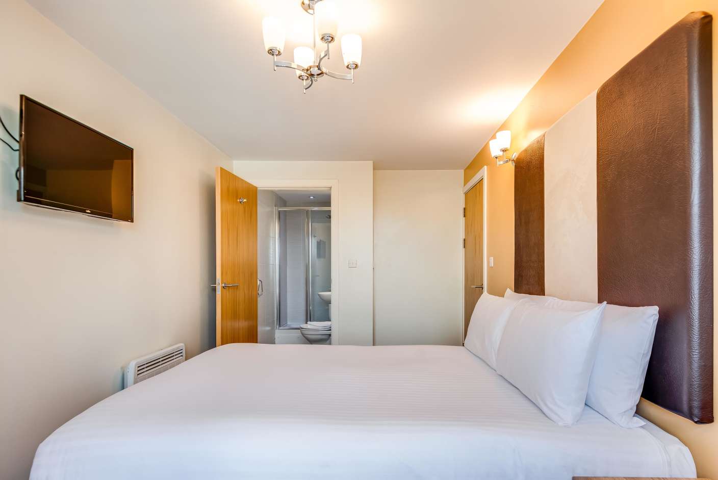 King size bed with brown faux leather headboard and TV mounted on wall