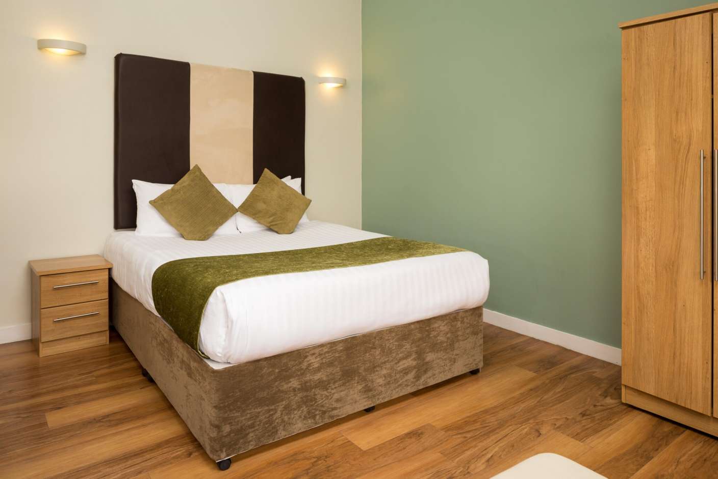 Studio apartment with king size bed, green cushions and bed dressings. 